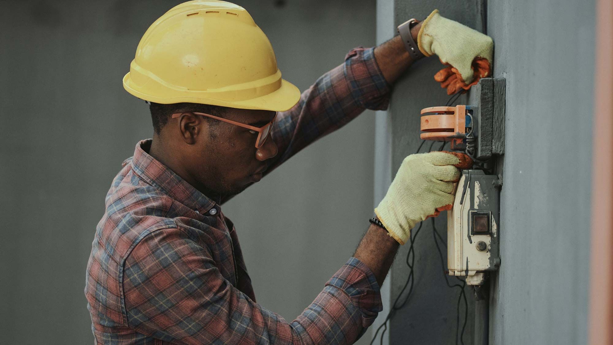 A technician in a yellow hard hat working on an outdoor electrical system.