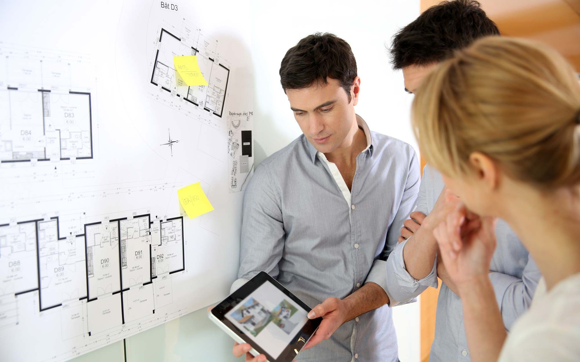 A group of professionals discussing a floor plan with tablet visuals.